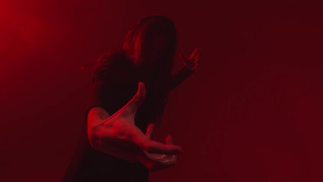 A fire mage with long hair and beard holds a burning hand pointed at the camera. Close up of the wizard's hand on which there is a real flame of fire