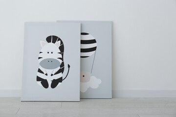 Adorable pictures of zebra and air balloon on floor near white wall. Children's room interior elements