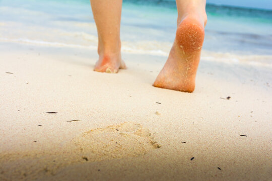 Girl's barefoot feet walking on white sandy caribbean beach