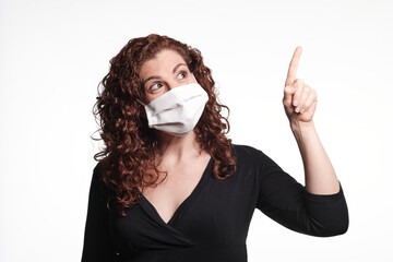 Redhead woman wearing a protective mask for coronavirus and pointing up with her finger