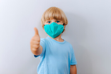 COVID-19 Optimistic kid boy wearing protective mask avoiding Coronavirus disease 2019 showing thumb up in white background. Covid-19 coronavirus