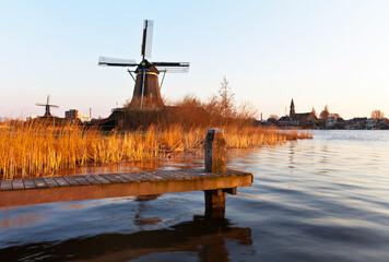 Beautiful Dutch landscape with a old windmill and a wooden pier on the Zaan River on sunset. Zaanse Schans Village. Netherlands