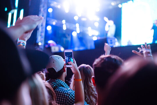 Hand with a smartphone records live music festival, Taking photo of concert stage. Youth, party, vacation concept.