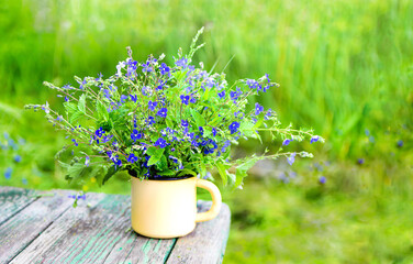 summer concept Fresh bouquet of blue flowers in a yellow mug, on the background of old boards and green grass. Copy space