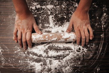 Rolling pin and flour on a wooden table. Cook holds a rolling pin. View from above. Close-up photo