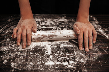 The cook holds a rolling pin on the table in flour. Close-up photo