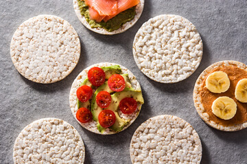 Puffed rice cakes with guacamole salmon,tomato and avocado, and banana with peanut butter on gray stone background. Top view