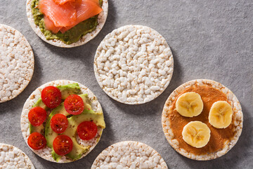 Puffed rice cakes with guacamole salmon,tomato and avocado, and banana with peanut butter on gray stone background. Top view