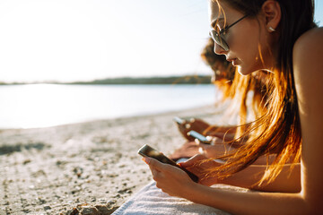 Three girls with a phone on the beach. Young girls sunbathe and take photo. Beach holiday and summer vacation concept.