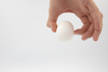 Fototapeta na wymiar a white egg holds with two fingers a male hand on a white background 