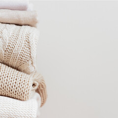 Fototapeta na wymiar Close up stack of neatly folded warm knitted woolen sweaters on a beige background. Capsule wardrobe, wardrobe, minimalism, knitted texture, order, comfort, macro. Square with copy space for text.