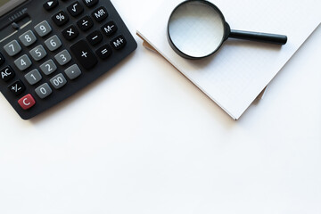 Workplace with notebook, magnifying glass and calculator on white backround. Copy space. Top view. Concept business.