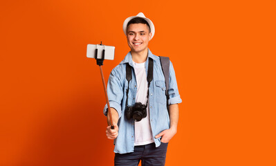 Positive guy tourist taking selfies with smartphone and selfie stick