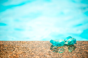 Close-up of waterproof children's swimming goggles lie on a wooden surface against the background of a blurred pool on a warm summer day. Concept of vacation with children at sea. Advertising space
