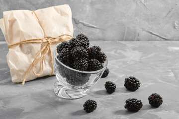 Fototapeta na wymiar A small glass cup filled with blackberries. Close-up, ripe blackberry berries on a gray background Delivery of products, copies of space, photos for the catalog of stores.