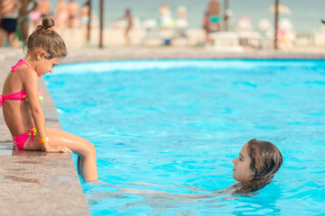 Side view little girls sisters swim in the pool and splashes water on each other during a vacation in a tropical country on a sunny warm summer day. Children rest concept