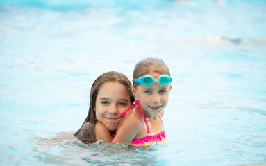 Two cute little sisters girls swim in the pool during vacation on a sunny warm summer day. The concept of the long-awaited vacation. Advertising space