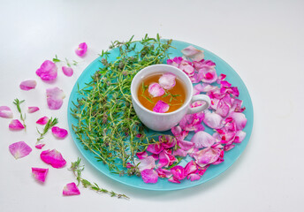 Homemade herbal tea in a white cup. Tea rose petals and thyme on a plate - ingredients for hot healthy drink 