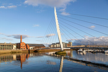 Fototapeta premium The Millennium footbridge over the River Tawe at Swansea Marina in the popular SA1 Maritime Quarter. Sailboats are moored in the marina.