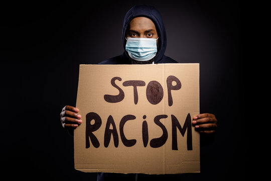 Photo of serious afro american guy hold card board banner stop racism share message human equality wear jumper medical mask isolated over black color background