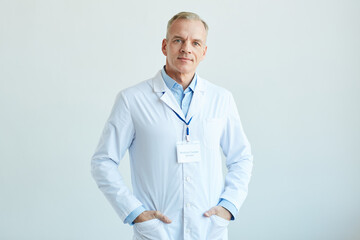 Waist up portrait of confident mature doctor wearing lab coat and looking at camera while standing...