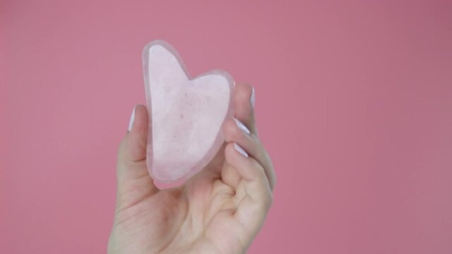 Pink quart gua sha in a woman's hand on blue background, a copy of the space