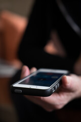 Hand holding mobile in the direction of the camera, with dark background and narrow depth of field