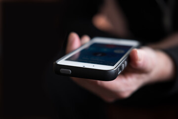 Hand holding mobile in the direction of the camera, with dark background and narrow depth of field