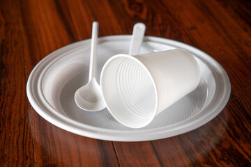 Utensilios de plástico blanco desechables para comer y beber, sobre mesa de madera.