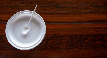 Plato y cuchara de plástico blanco desechables sobre madera oscura