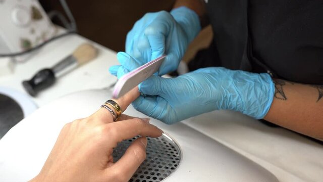 Aesthetician doing the manicure, filing the nails with a file to his client in a beauty center