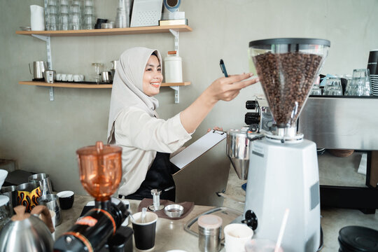 female waiter holds a machine coffee to check the stock of raw materials for the cafe
