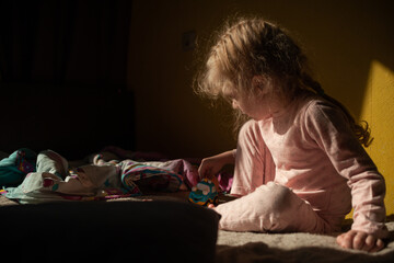 Portrait of a playing girl at home in the sun on a yellow wall