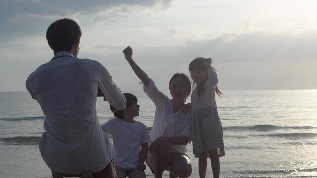 Happy asian family taking a picture with phone on the beach in vacation together, parents and children go to travel taking a photo for leisure and activity in summer, lifestyle concept.