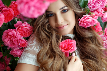 Beautiful portrait of a woman in poses. A brunette woman is standing next to roses in nature.