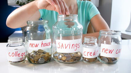 Young woman spreading her money savings in glass jars. Concept of financial investment, economy growth and bank savings