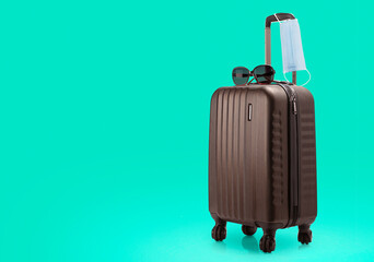 Concept of pandemic travel. Suitcase with sunglasses and mask isolated on green medical background. Left side is made for placing copy