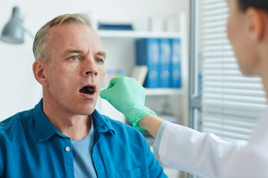 Unrecognizable female doctor taking swab sample from mouth and throat of mature man for virus test in clinic, copy space - Powered by Adobe
