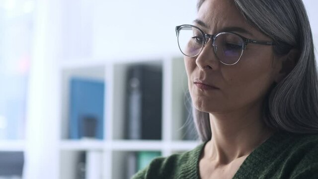 A close-up view of a mature woman-worker is putting off her eyeglasses in the office