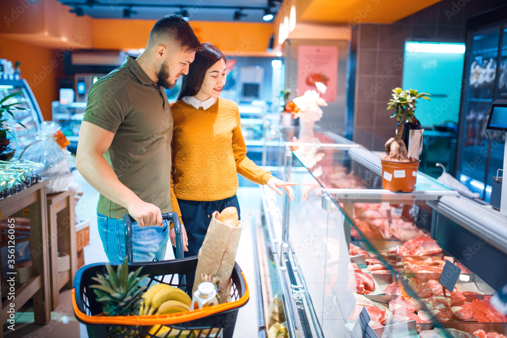 Wall mural couple choosing fresh chilled meat, grocery store