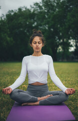 Young woman meditating in the green morning park. Relax yoga pose. Yoga and relaxation concept.