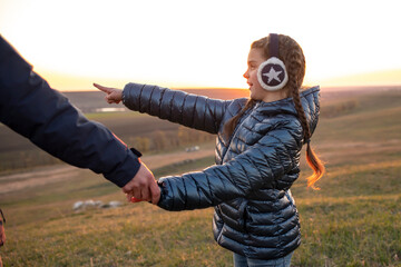 A girl holds dad by the hand and points into the distance.