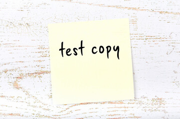 Yellow sticky note on wooden wall with handwritten word test copy - obrazy, fototapety, plakaty