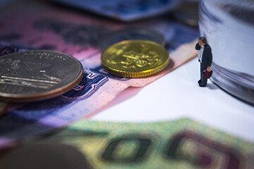 The miniature business man standing at near the transparent paper weghit with banknotes and coins on the white table in spooky mood.