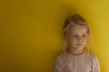  Portrait of a little offended girl. Dissatisfied girl on a background of yellow wall