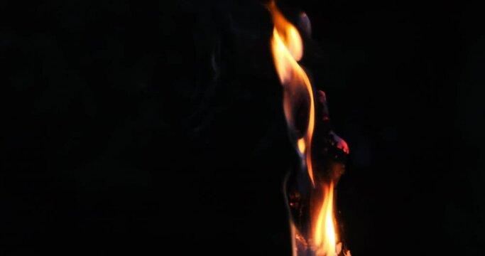 Close up shot of a firestick, torch, flambeau with fire, lights, red sparks in slow motion on a dark environment. 4k video of old wood on orange fire, destruction emitting smoke in natural surrounding