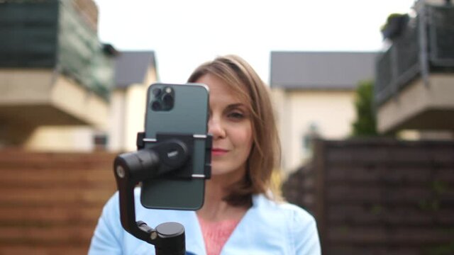 A woman is recording video using a smartphone with a stabilizer. Social media and video blogging, outdoor portrait woman with smartphone