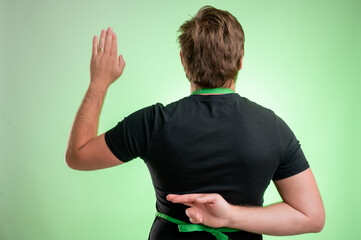 Supermarket employee with green apron and black t-shirt showing fake oath cross finger from behind