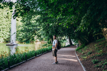 Sofia Park, Uman. Handsome man with beard and backpack on a park tour. A man in a T-shirt and shorts walks along the lake embankment with a fountain.
