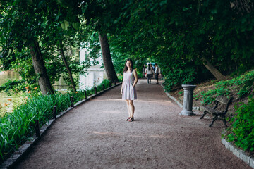 Fototapeta na wymiar Sofia Park, Uman. Girl in a summer board on the alley of the park. Smiling brunette girl on a stone alley near the lake. Walk in the park, a large beautiful lake.